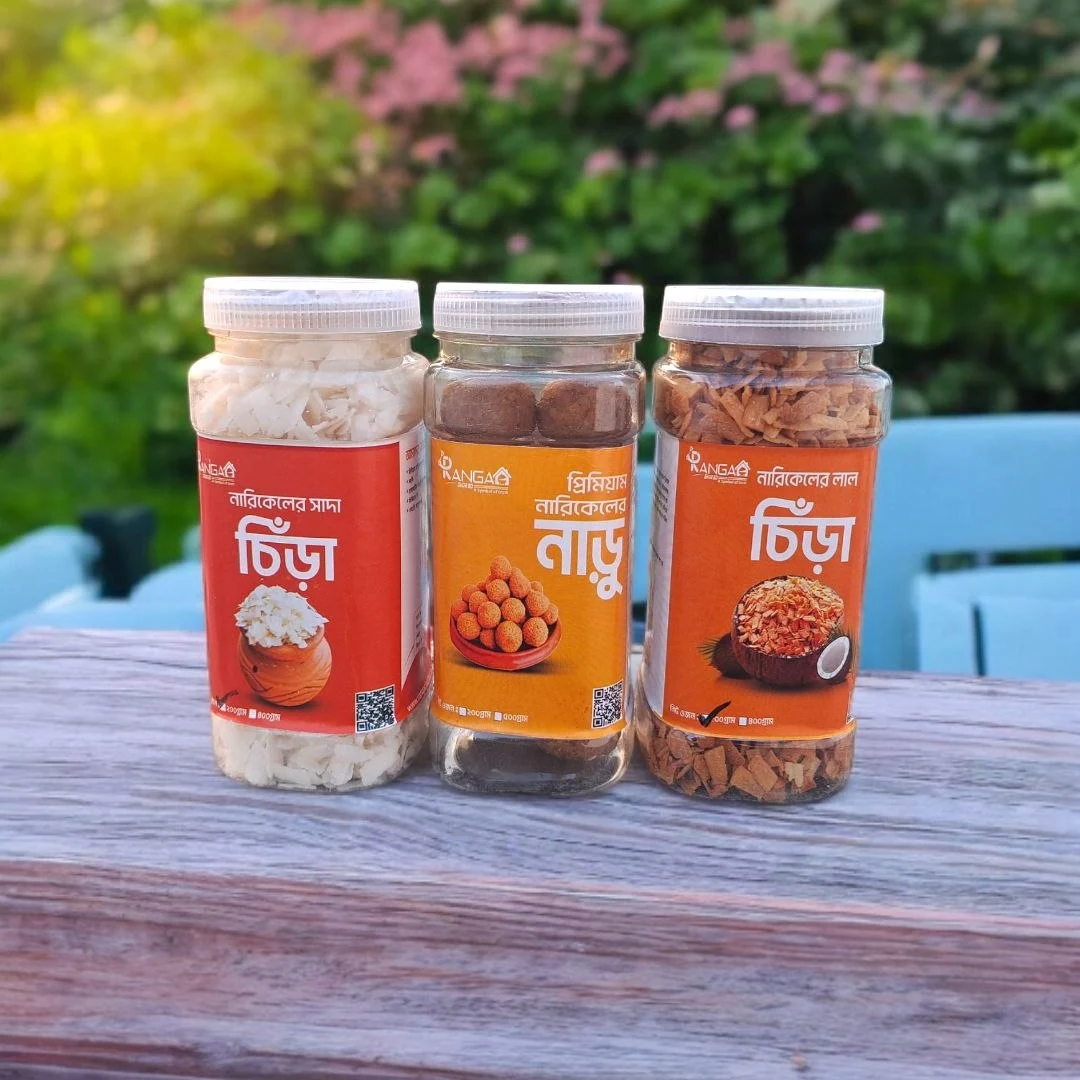 রাঙ্গাঘরের নারিকেল নাড়ু ও চিঁড়ার তিনটি জার সবুজ বাগানে কাঠের টেবিলে সাজানো